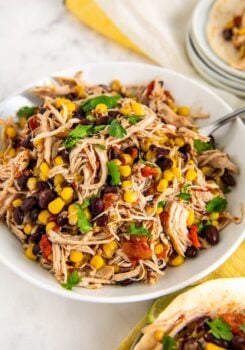 A large serving bowl of juicy slow cooker Mexican chicken with rotel with a large spoon on the side and fresh cilantro sprinkled on top.