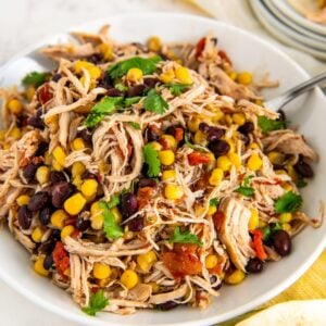 A large serving bowl of juicy slow cooker Mexican chicken with rotel with a large spoon on the side and fresh cilantro sprinkled on top.