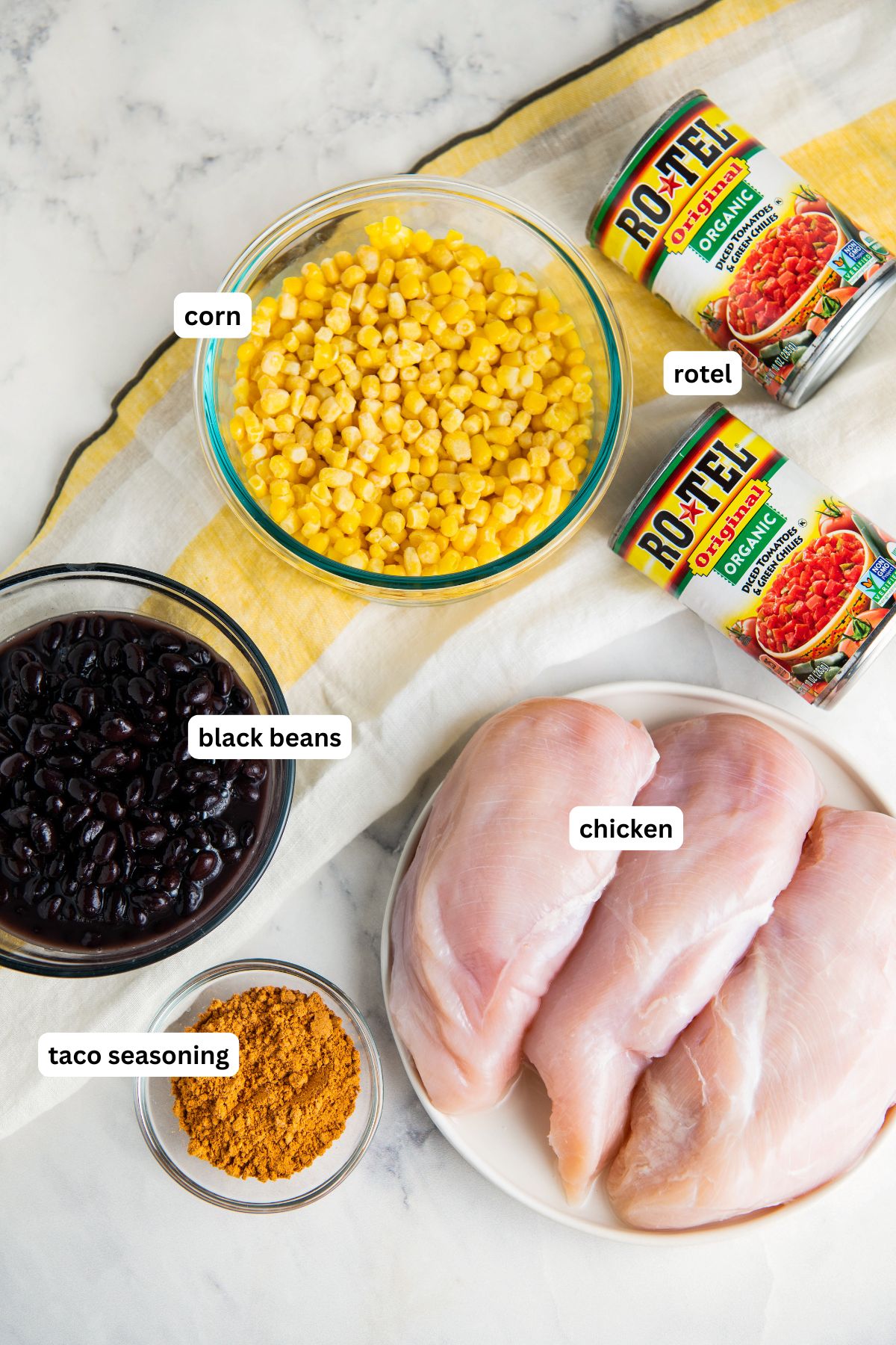 Ingredients for slow cooker mexican chicken recipe arranged in bowls. From top to bottom: rotel, corn, black beans, chicken breasts and taco seasoning.