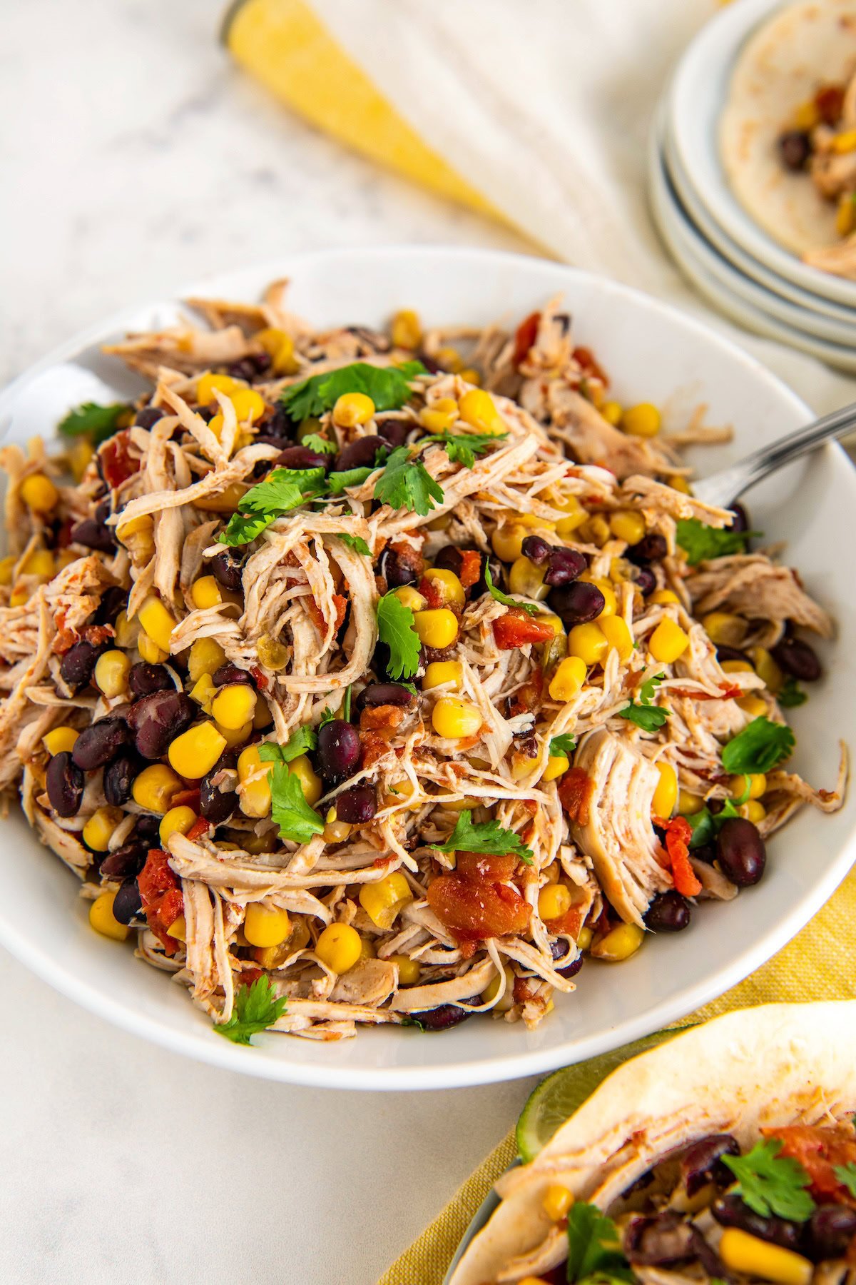 A large serving bowl of juicy slow cooker Mexican chicken with rotel with a large spoon on the side and fresh cilantro sprinkled on top.