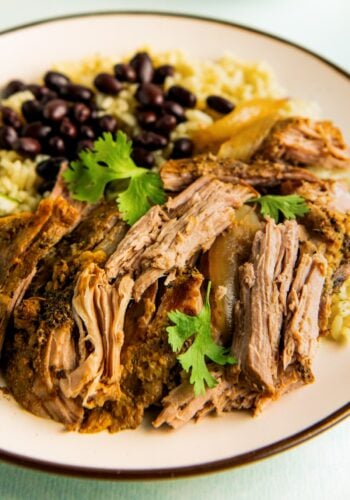 Tender bites of shredded mojo pork are plated with rice and beans.