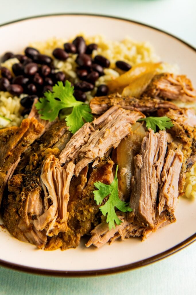 Tender bites of shredded mojo pork are plated with rice and beans.