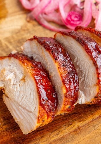 Sliced oven baked bbq chicken coated in sweet and savory bbq sauce on a wooden cutting board.