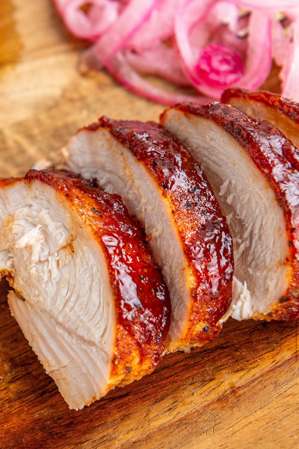 Sliced oven baked bbq chicken coated in sweet and savory bbq sauce on a wooden cutting board.