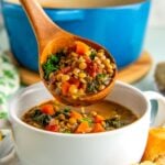 A wooden ladle spooning vegetarian lentil soup into a bowl with crusty bread on the side.