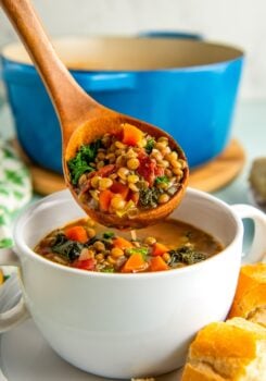 A wooden ladle spooning vegetarian lentil soup into a bowl with crusty bread on the side.