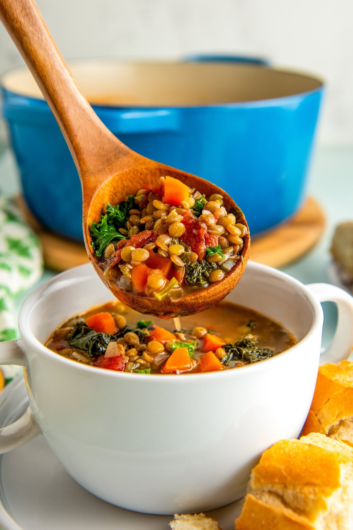 A wooden ladle spooning vegetarian lentil soup into a bowl with crusty bread on the side.