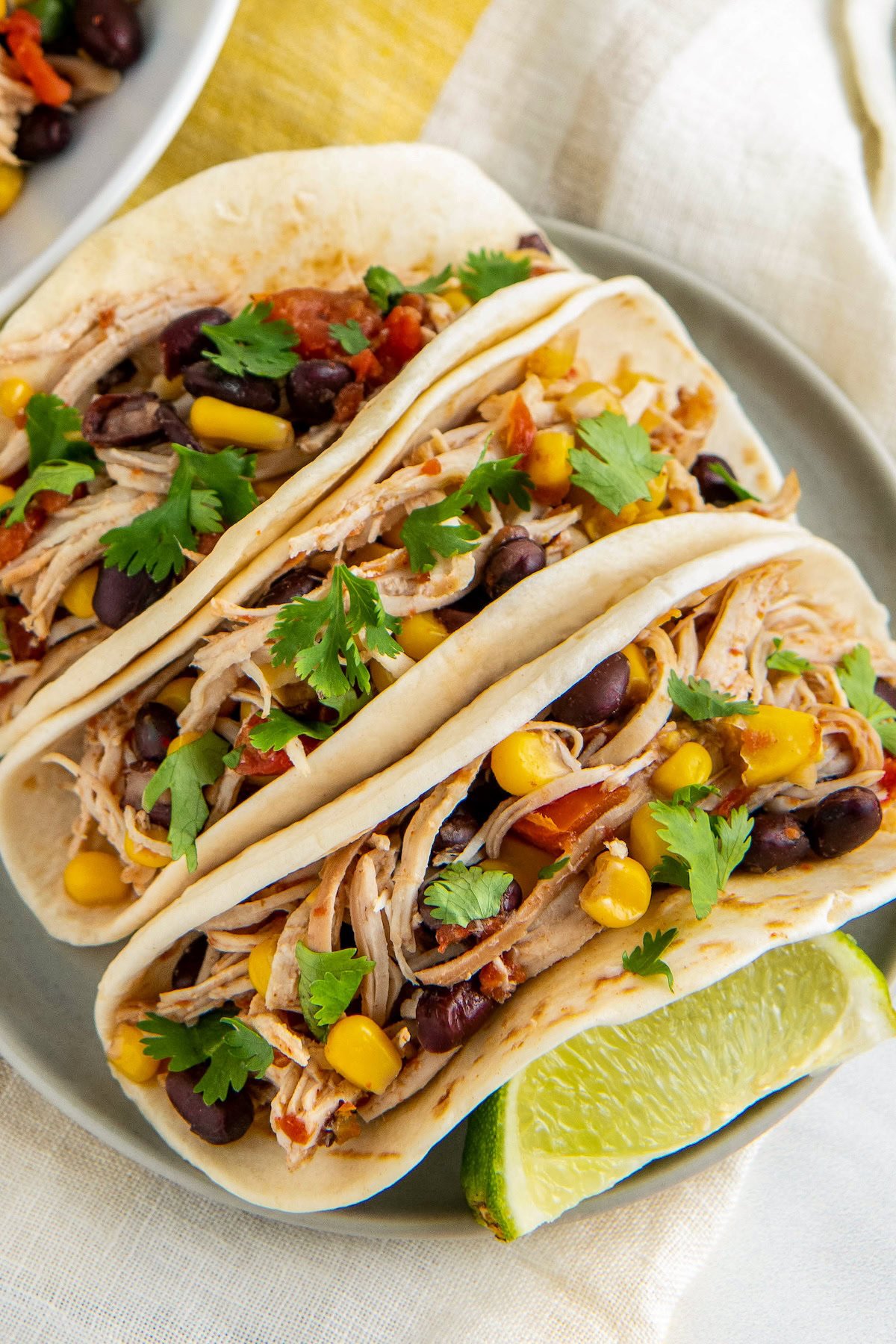 Crockpot shredded mexican chicken with black beans and corn served in warm flour tortillas with a lime wedge on the side.