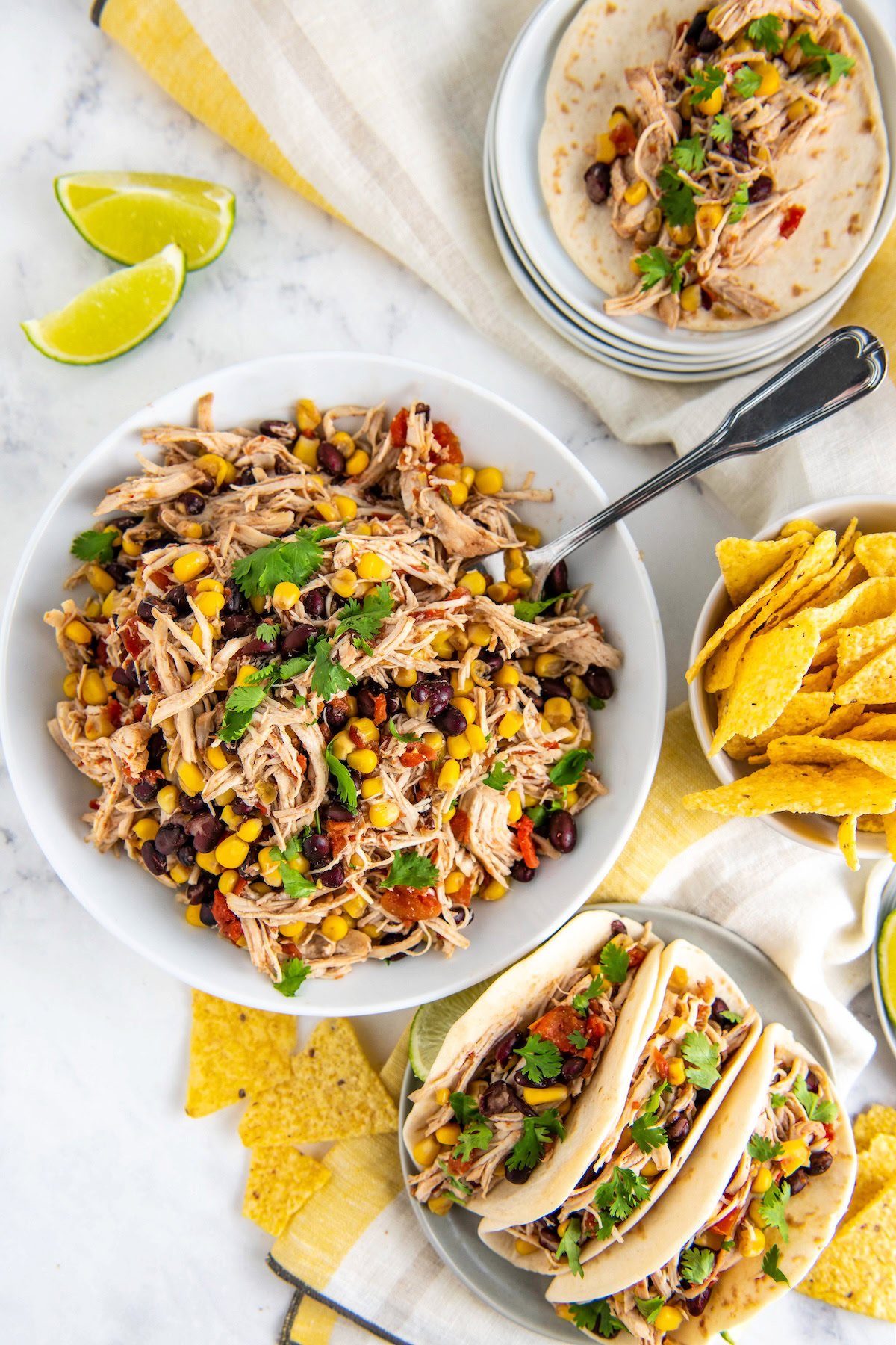 Crockpot Mexican Chicken in a bowl with a serving spoon and the shredded Mexican chicken served in flour tortillas with cheese and cilantro on top.