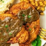 Breaded pork chops and gravy on a plate with corn and mashed potatoes.