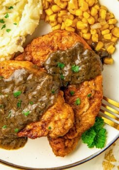 Breaded pork chops and gravy on a plate with corn and mashed potatoes.