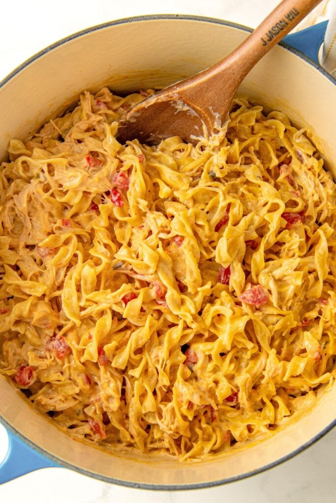 Cheesy rotel chicken pasta mixing in a bowl with a wooden spoon.