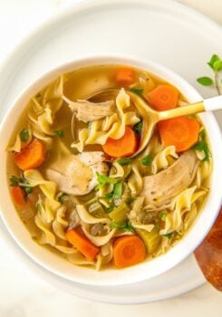 A spoon is digging into a bowl of crockpot chicken noodle soup.