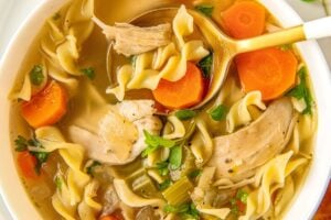 A spoon is digging into a bowl of crockpot chicken noodle soup.