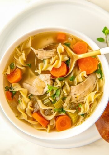 A spoon is digging into a bowl of crockpot chicken noodle soup.