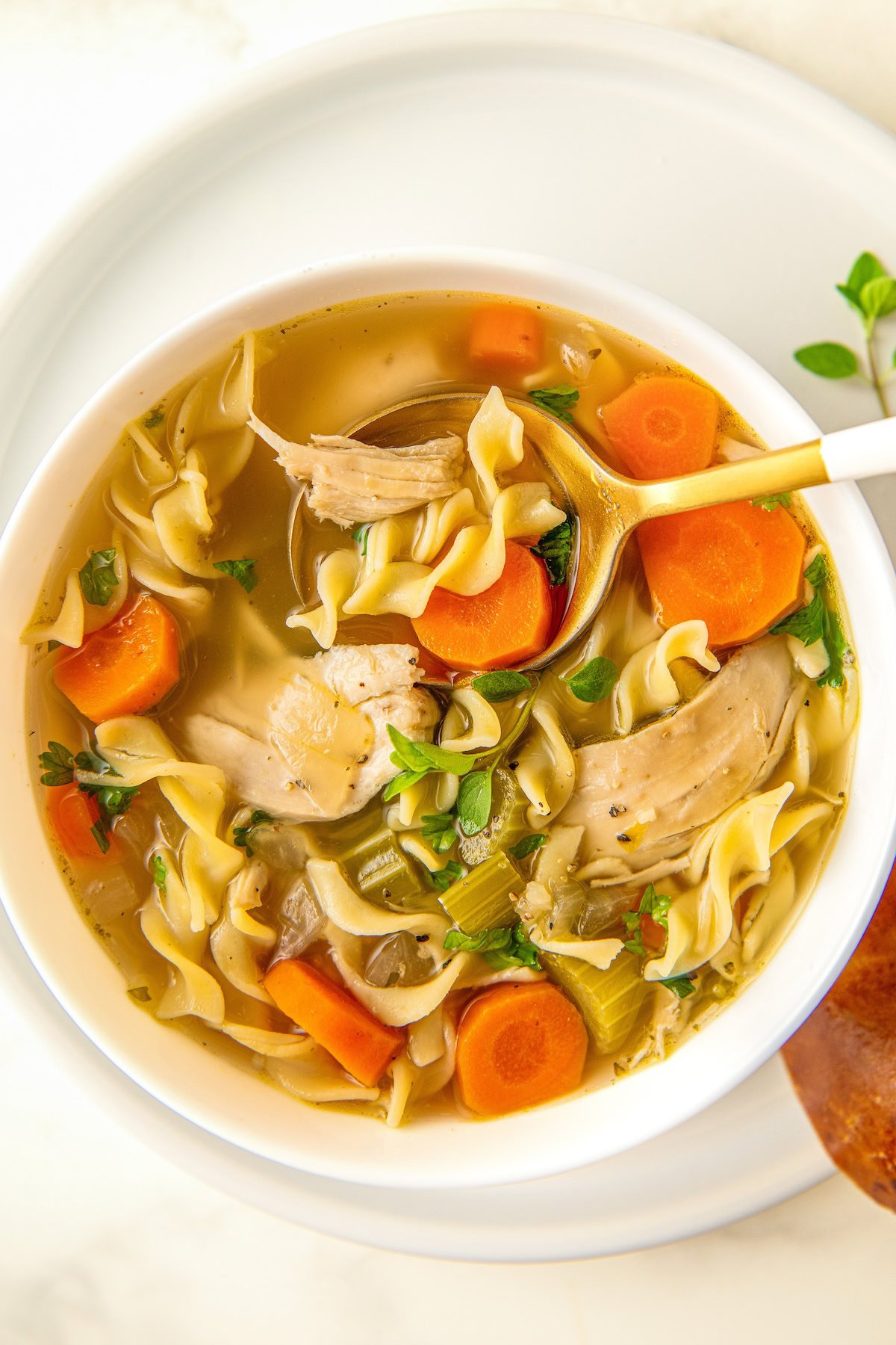 A spoon is digging into a bowl of crock pot chicken noodle soup with egg noodles and tender vegetables. 