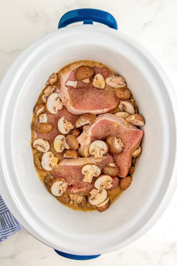 Mushrooms and seasoned pork chops have been added on top of gravy in slow cooker.