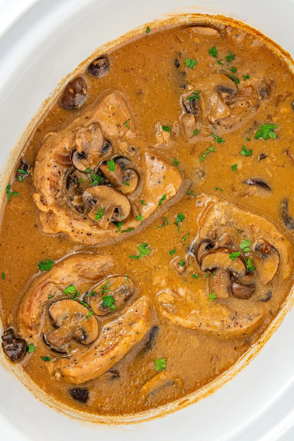 A crockpot is filled with gravy smothered pork chops. 