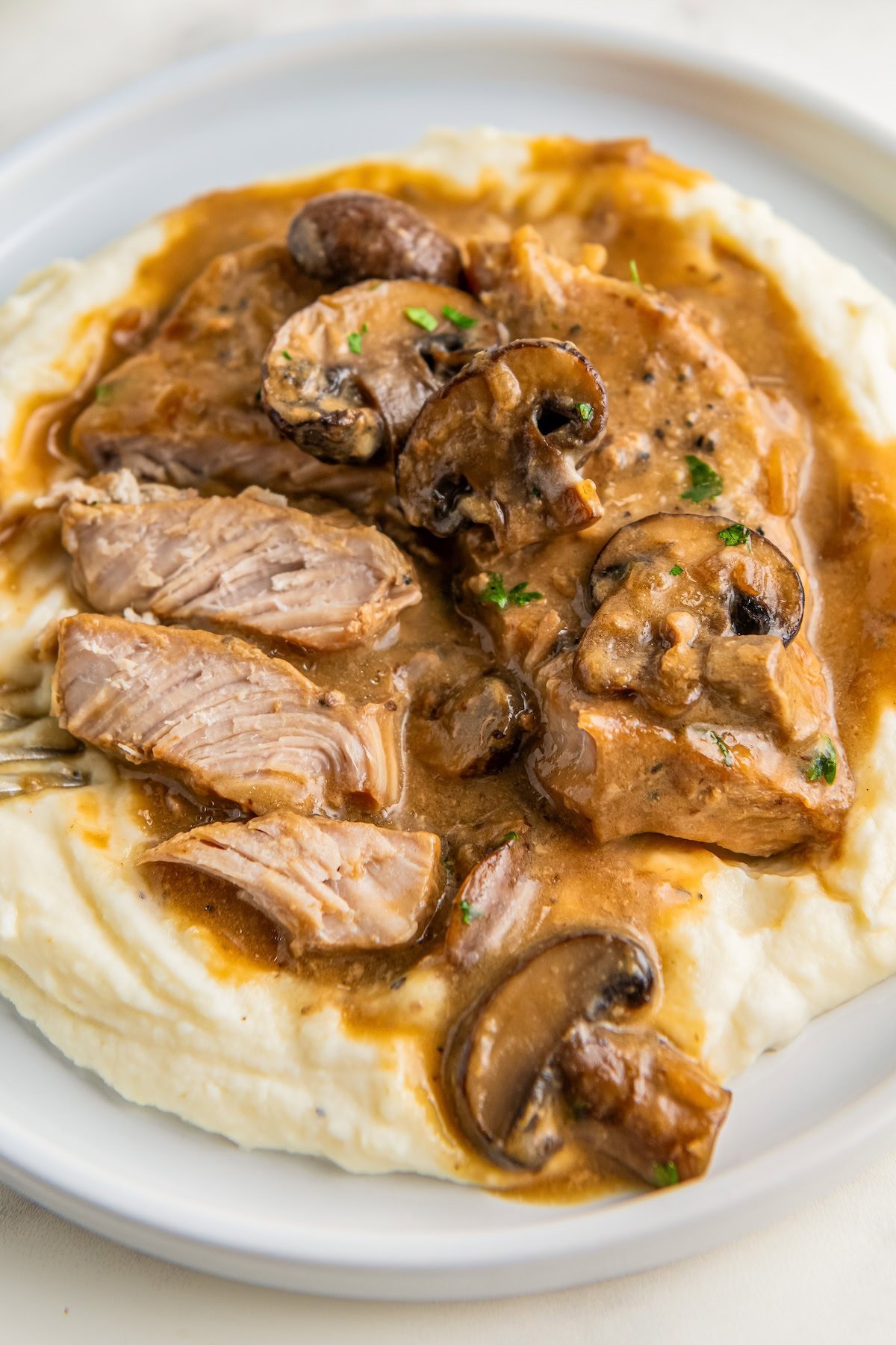 Sliced pork chops with mushroom soup gravy on a plate with mashed potatoes. 