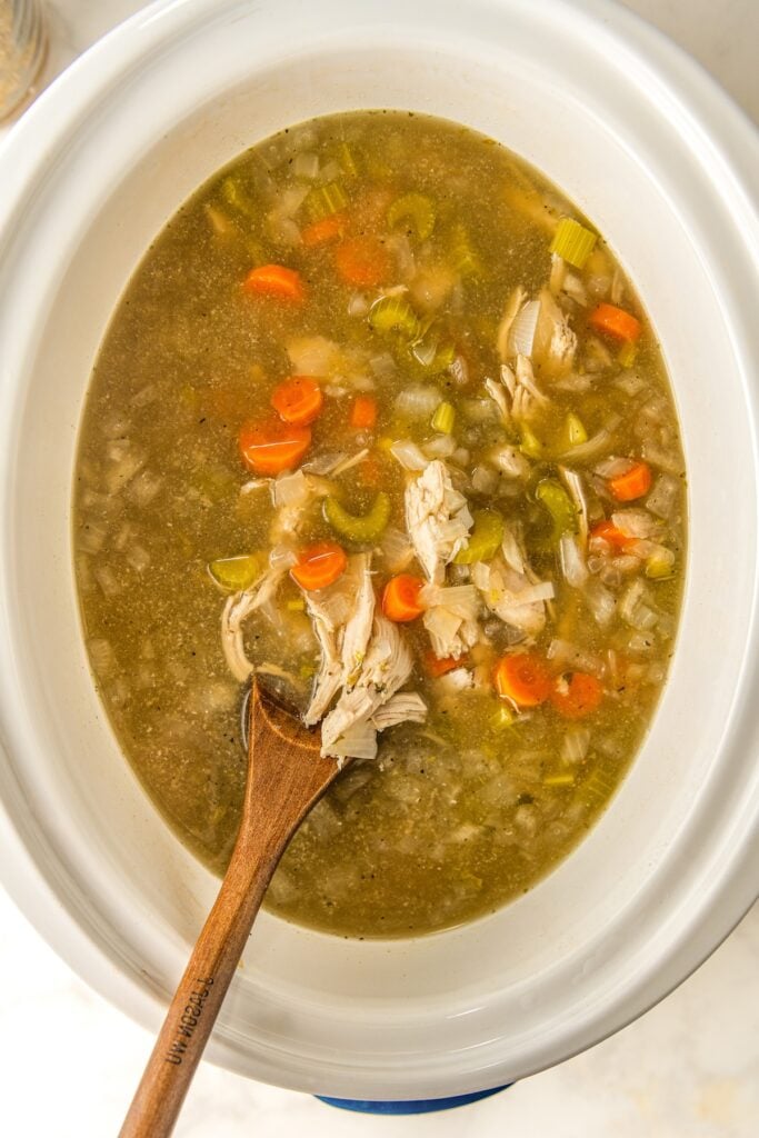 Chicken soup in a crock pot with chicken being shredded.