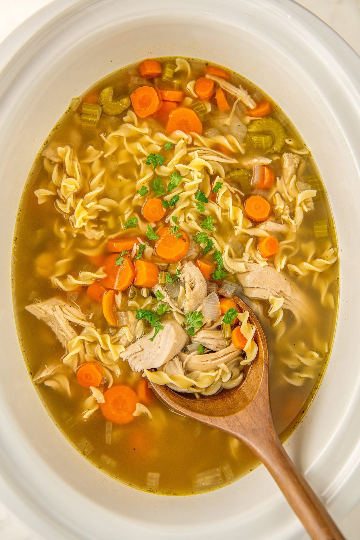 Chicken noodle soup in crock pot with a wooden spoon for serving.