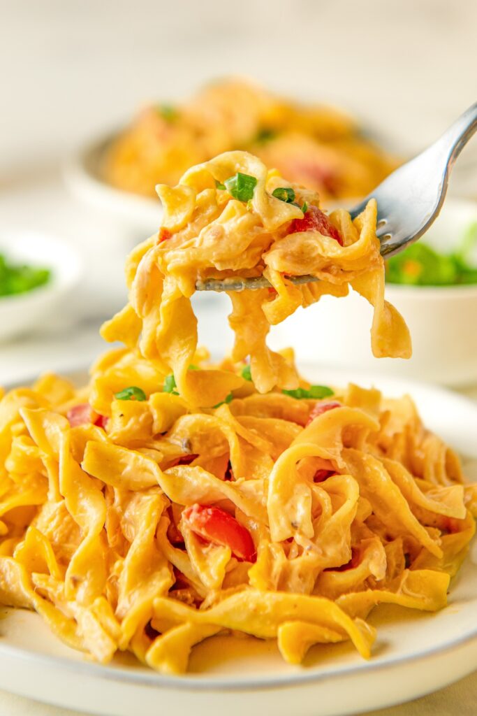 A forkful of cheesy chicken rotel pasta is held above a full plate.