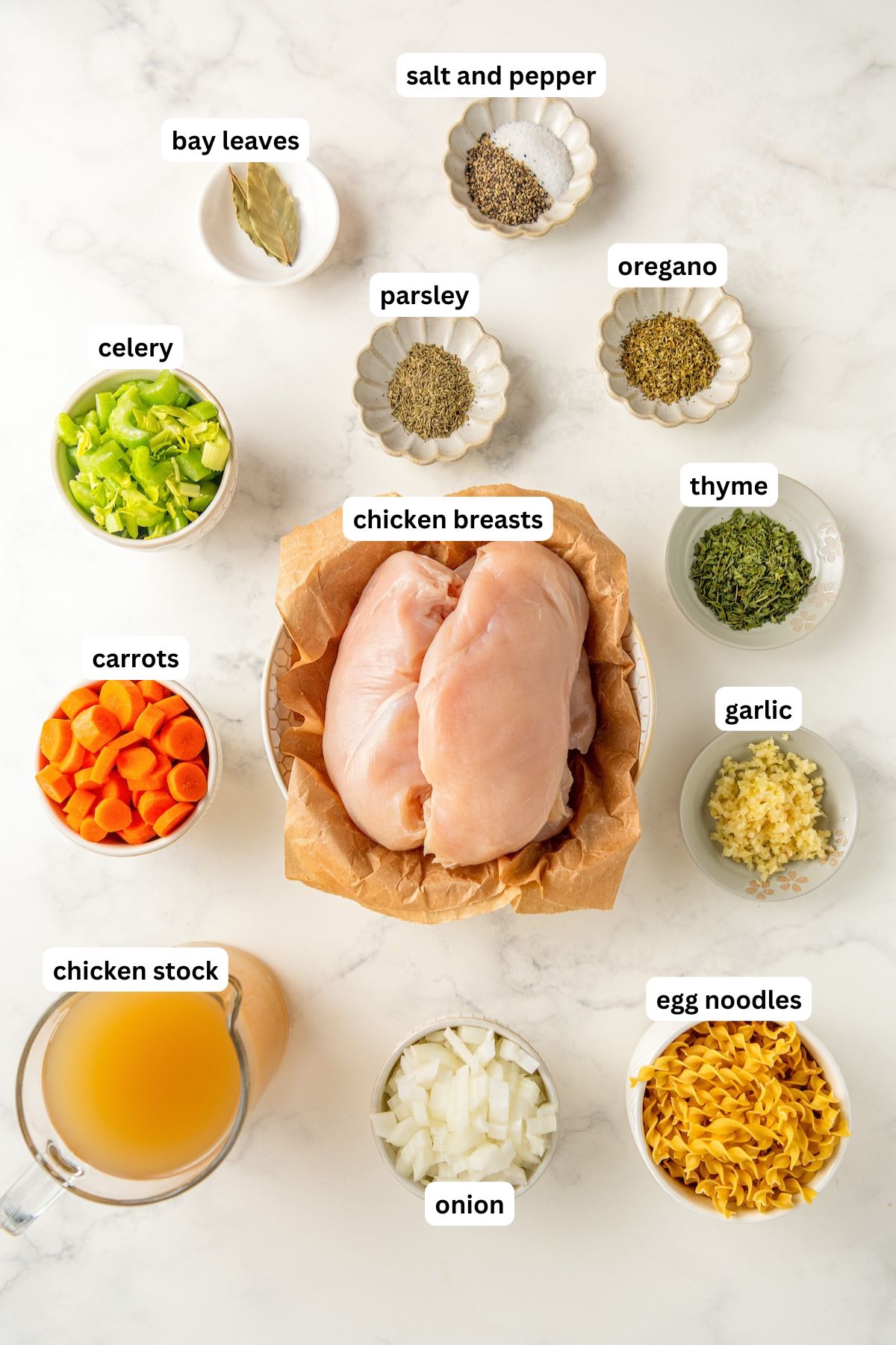 The ingredients for crockpot chicken noodle soup recipe in order from top to bottom: bay leaves, salt and pepper, celery, parsley, oregano, thyme, carrots, chicken breasts, garlic, chicken stock, onion and egg noodles.