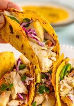 An air fryer fish taco with slaw is lifted from the plate.