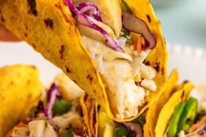 An air fryer fish taco with slaw is lifted from the plate.