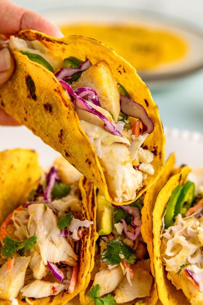 An air fryer fish taco with slaw is lifted from the plate.