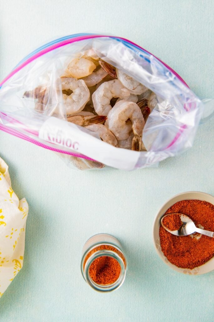 Raw shrimp in a ziplock bag next to a container of spices.