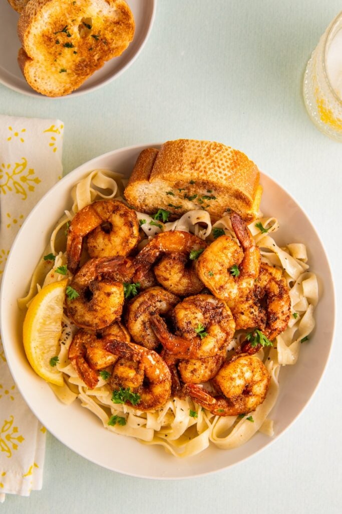 Blackened shrimp served on top of pasta with toasted bread and a lemon wedge on the side.