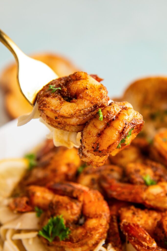 A fork is lifting a portion of seasoned shrimp from the plate.