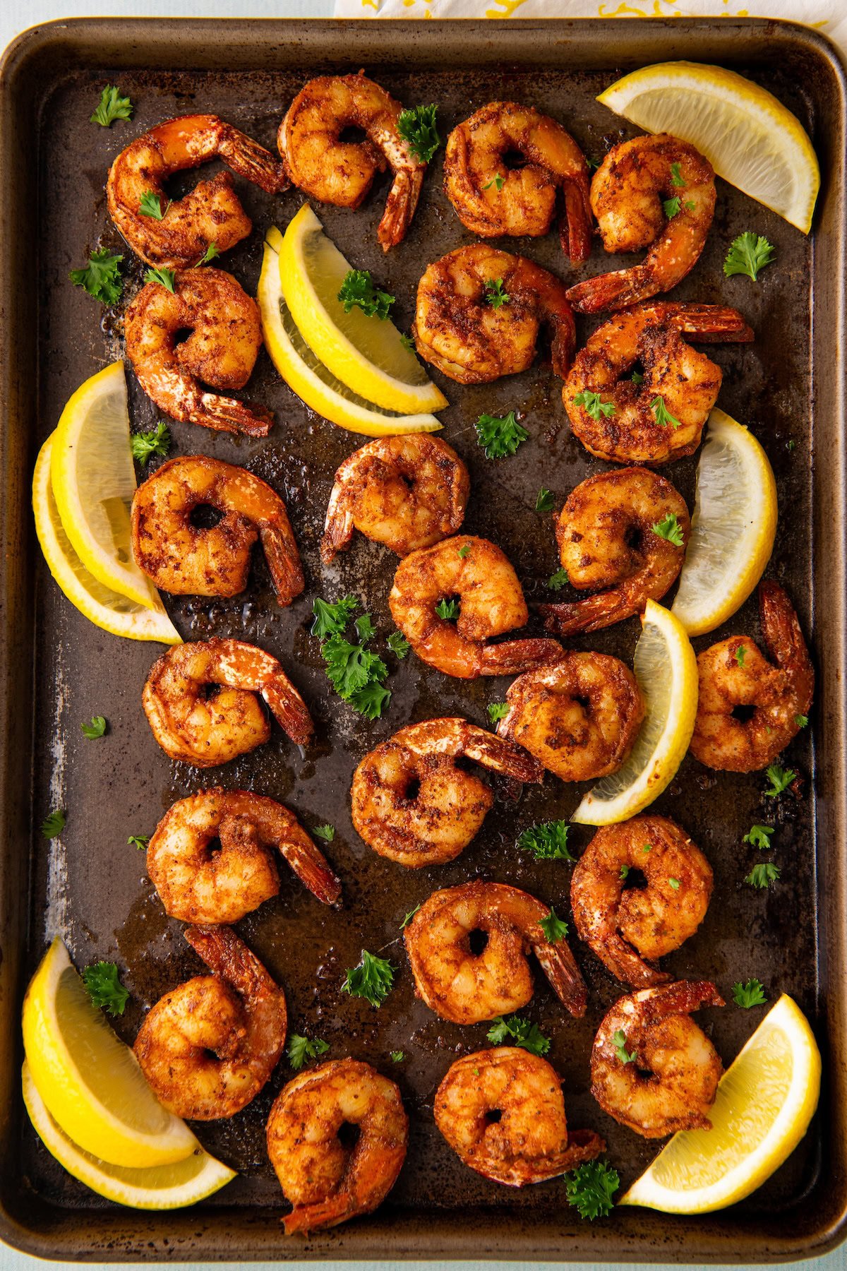 Cooked shrimp on a sheet pan coated in blackening seasoning with lemon wedges and fresh parsley.