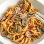 Creamy mushroom pasta with bacon, fresh parsley and grated parmesan cheese sprinkled on top in a bowl.