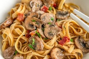 Creamy mushroom pasta with bacon, fresh parsley and grated parmesan cheese sprinkled on top in a bowl.