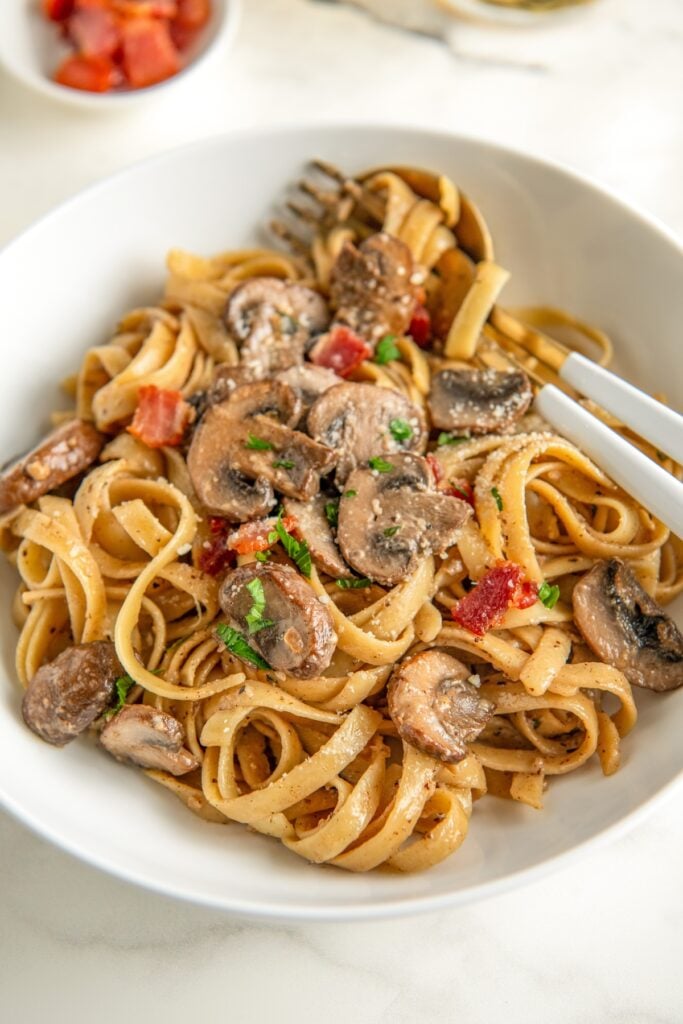 Creamy mushroom pasta with bacon, fresh parsley and grated parmesan cheese sprinkled on top in a bowl.