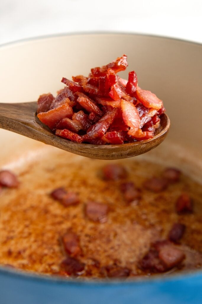 Sautéed bacon in a large pot being lifted out with a spoon.