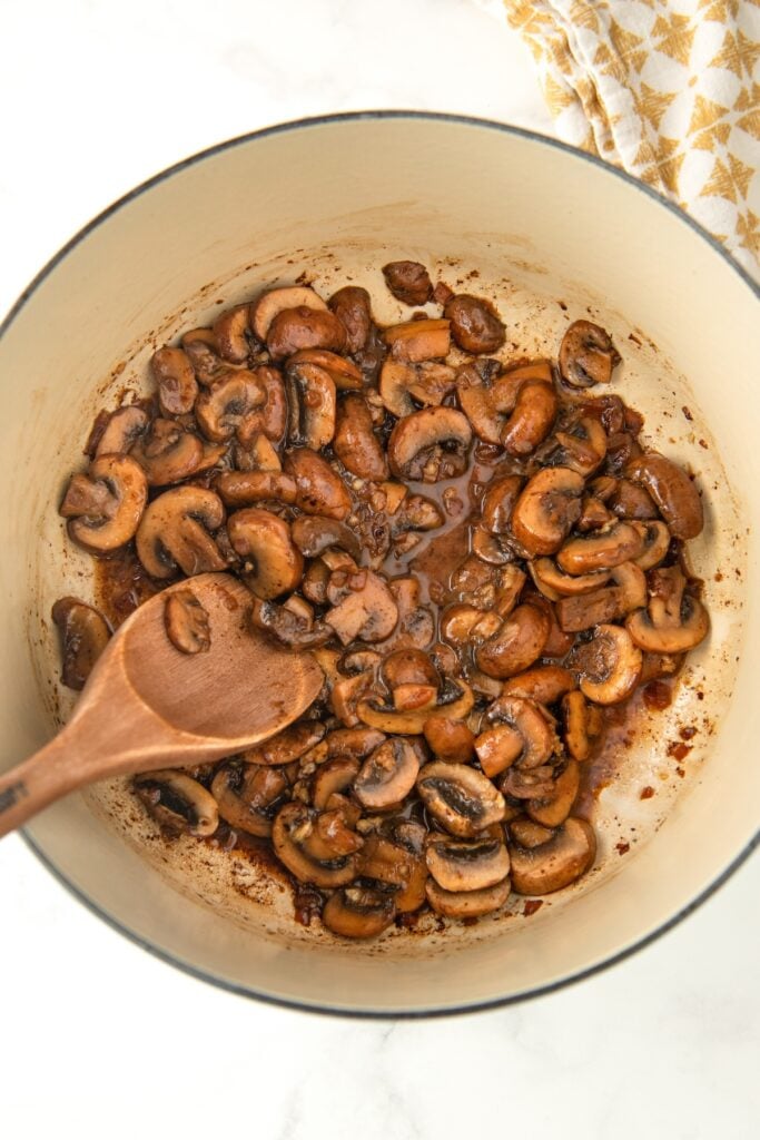 Sautéed mushrooms in a large pot with a wooden spoon.