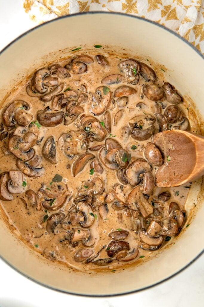 Sautéed mushrooms simmering in a rich cream sauce with fresh herbs being added.