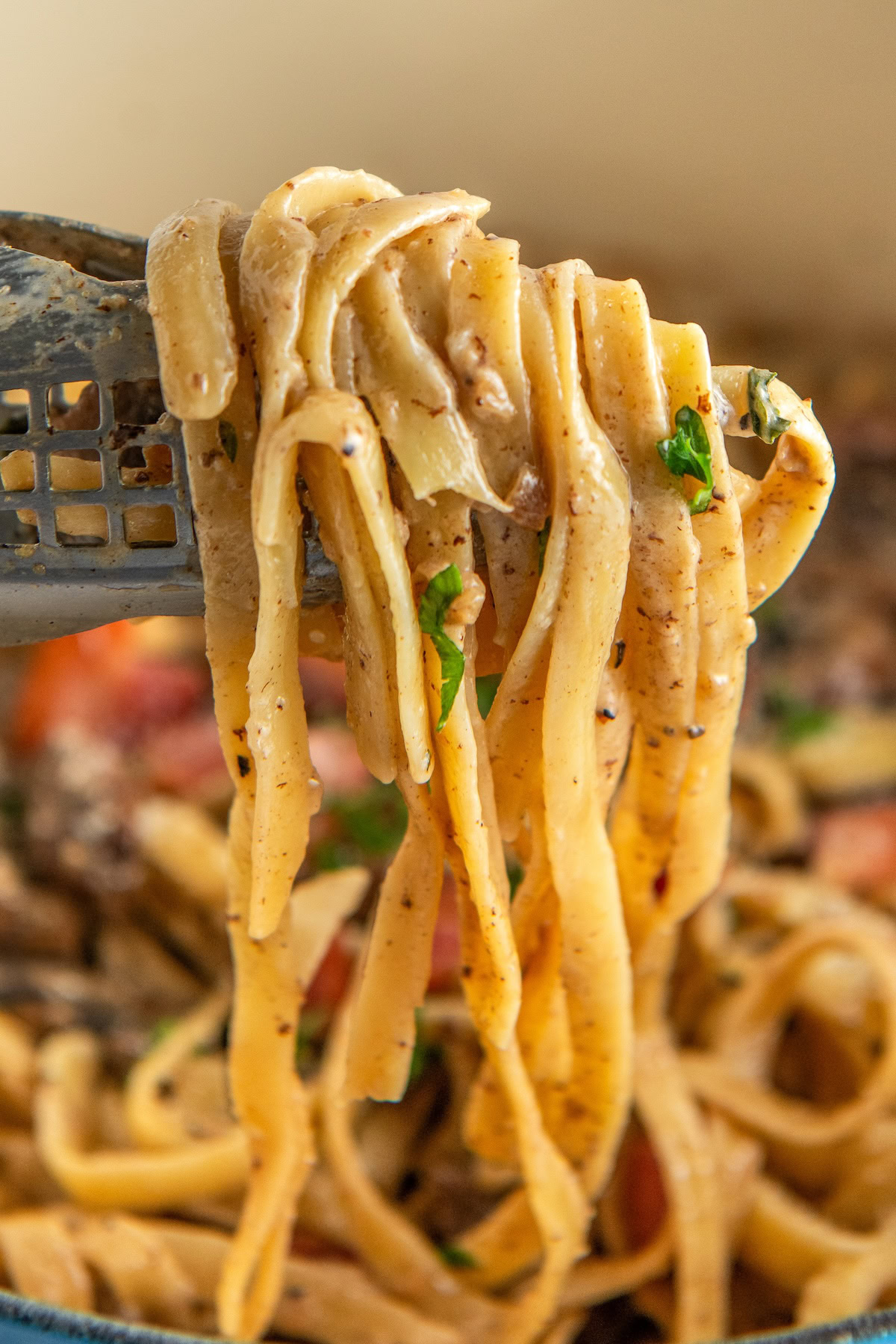 Creamy noodles coated in a mushroom pasta sauce being lifted out of a large pot with tongs.