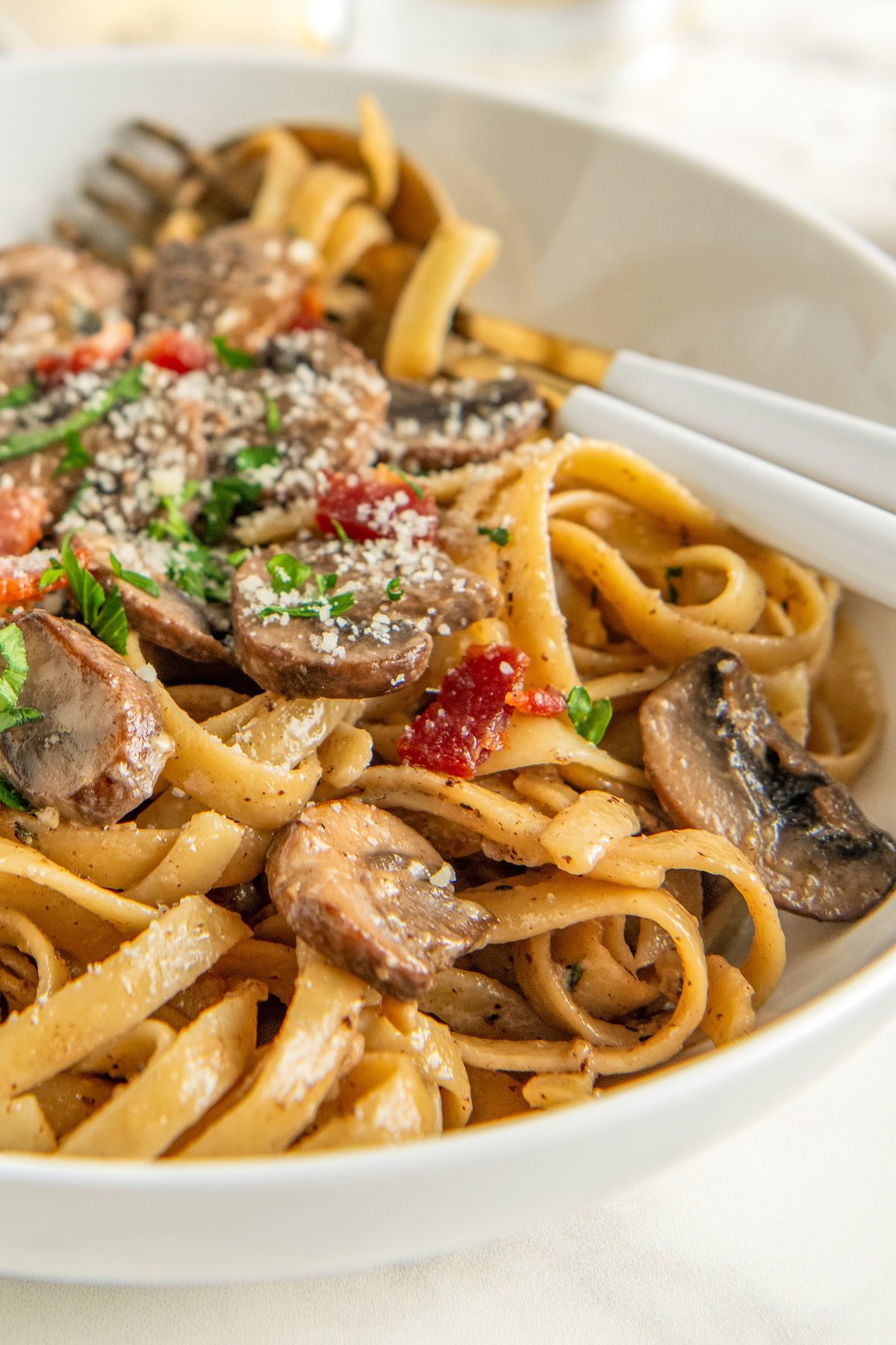 Rich and creamy mushroom pasta in a bowl garnished with fresh herbs, crispy bacon and parmesan cheese.