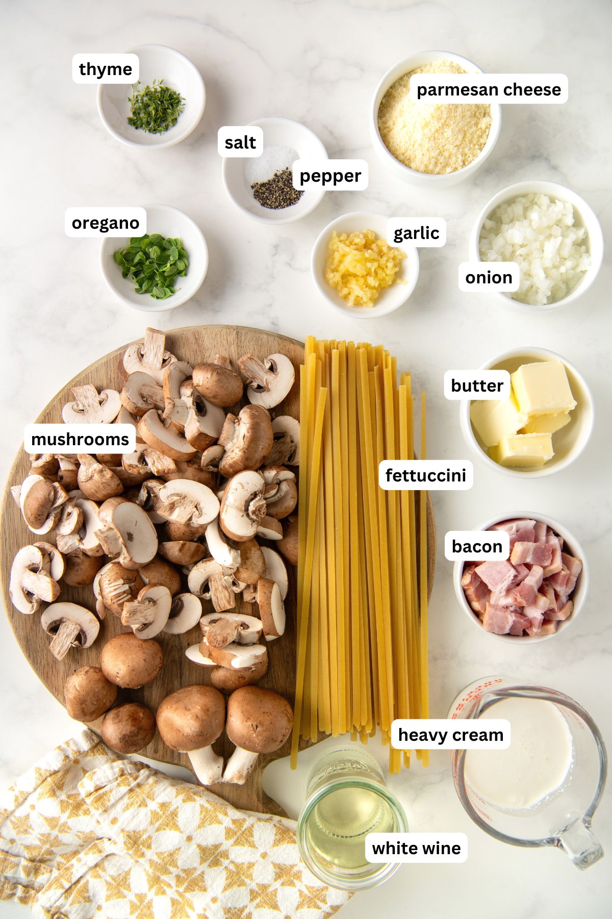 Ingredients for creamy mushroom pasta recipe from top to bottom: thyme, parmesan cheese, salt, pepper, oregano, garlic, onion, butter, mushrooms, fettuccini, bacon, heavy cream and white wine.