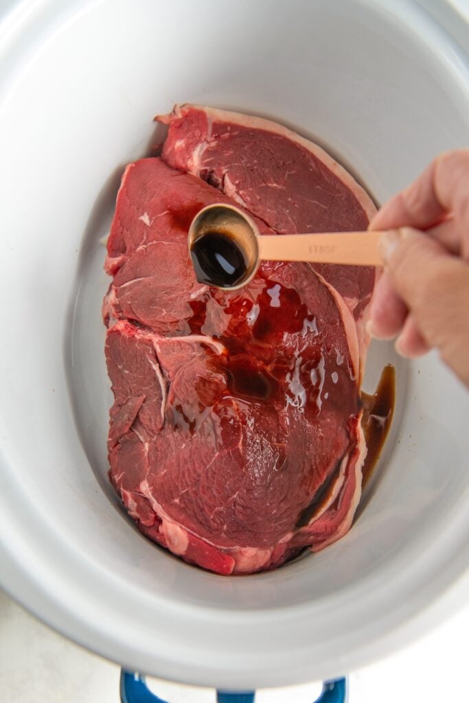 Worcestershire sauce is being added to steak in a slow cooker.