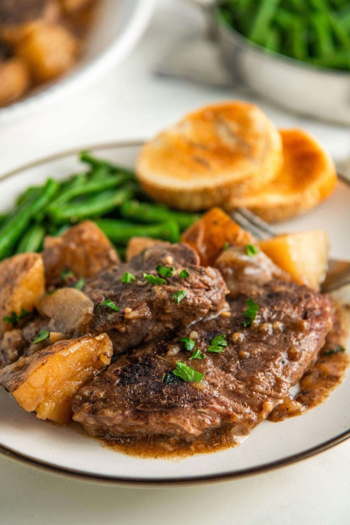 Savory, tender slow cooker steak and potatoes is plated with green beans and bread.