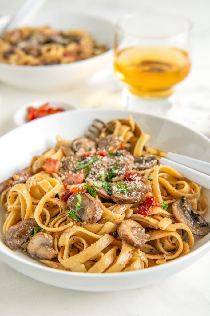 Two bowls filled with creamy mushroom pasta with bacon and topped with fresh parsley and parmesan cheese.