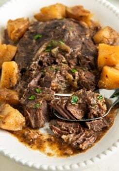 Fork tender steak with potatoes is plated on a white platter.