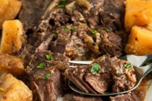 Fork tender steak with potatoes is plated on a white platter.