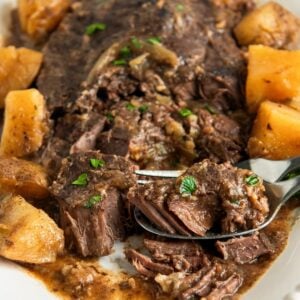 Fork tender steak with potatoes is plated on a white platter.