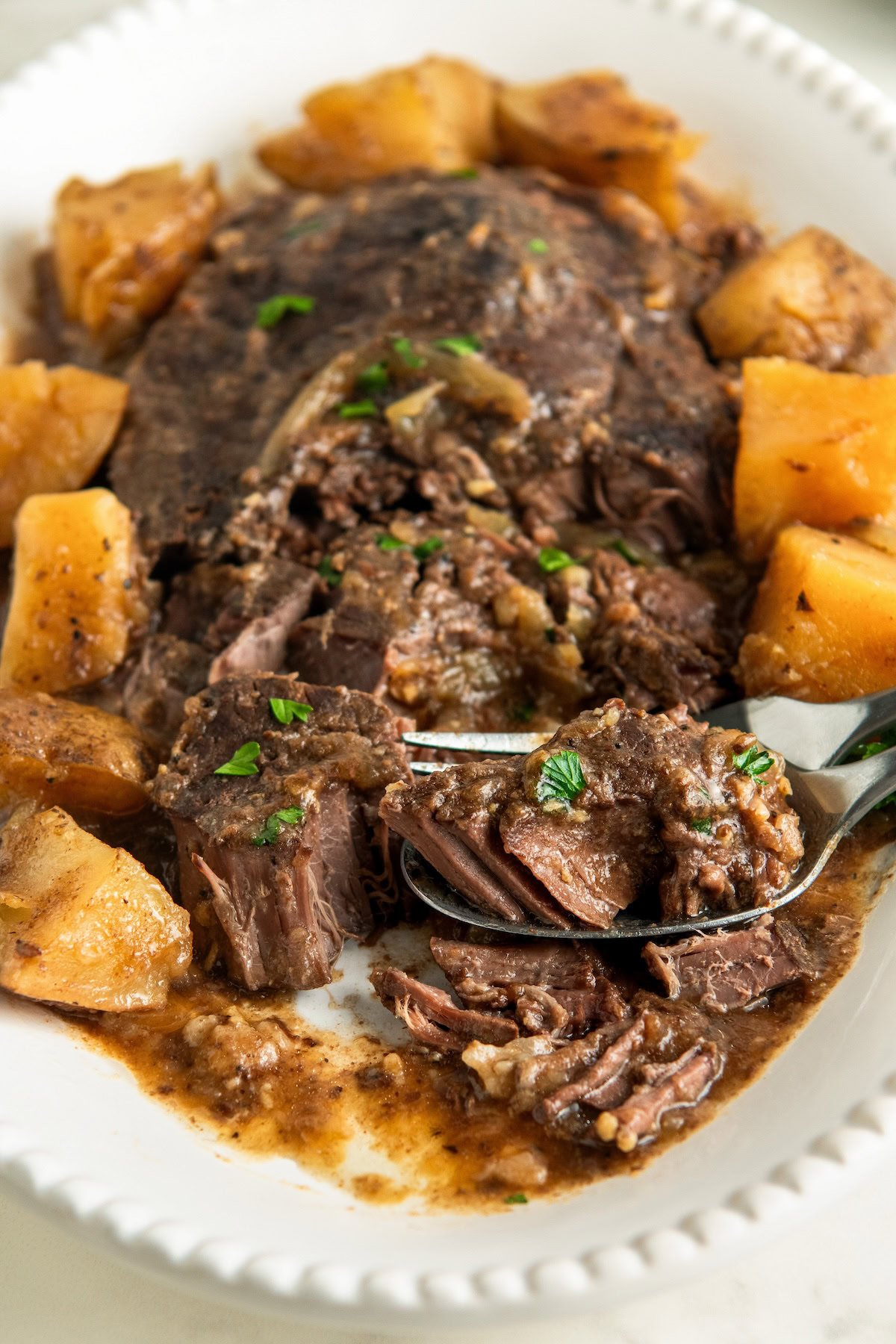 Fork tender steak with potatoes is plated on a white platter.